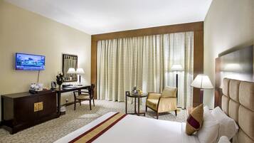 A hotel room with a bed, a desk, a television, and a window with curtains.
