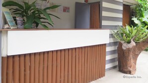 Een receptiebalie met een houten paneelontwerp, een grote kamerplant en een prikbord met diverse mededelingen.