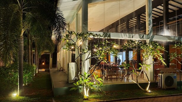A modern building with a covered outdoor seating area, surrounded by palm trees and well-lit by string lights. - Magampura Eco Village Resort (Thissamaharama)