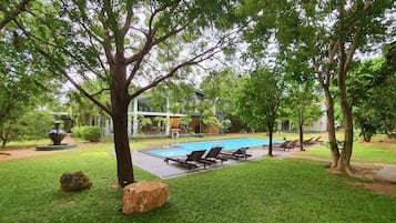 A swimming pool with lounge chairs, surrounded by trees and a grassy area.