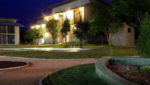 A two-story building with a well-lit exterior, a paved driveway, and a landscaped garden area. - Magampura Eco Village Resort (Thissamaharama)