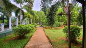 A pathway flanked by lush greenery and palm trees, leading to a central decorative feature. - Magampura Eco Village Resort (Thissamaharama)