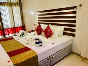 A neatly made bed with a striped headboard, a red and white pillow, and a blanket with a red stripe. - Magampura Eco Village Resort (Thissamaharama)
