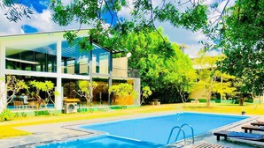 A swimming pool with lounge chairs and a modern building with large windows. - Magampura Eco Village Resort (Thissamaharama)