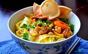 A bowl of noodle dish with vegetables and meat, accompanied by a piece of bread. - Quoc Thien Hotel (Da Nang)