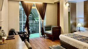 A hotel room with a bed, a desk, a chair, a ceiling fan, and a view of the outdoors. - Maya Inn (Gangtok)