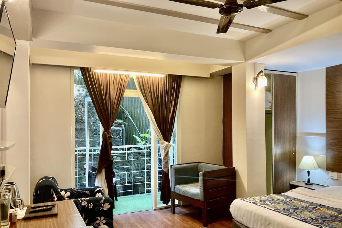 A hotel room with a bed, a desk, a chair, a ceiling fan, and a view of the outdoors.