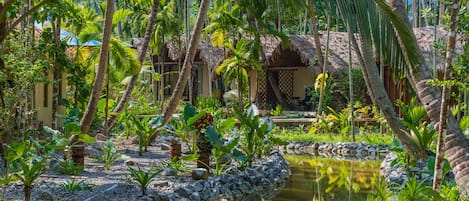 Un jardín tropical con un estanque, palmeras y una estructura con techo de paja.