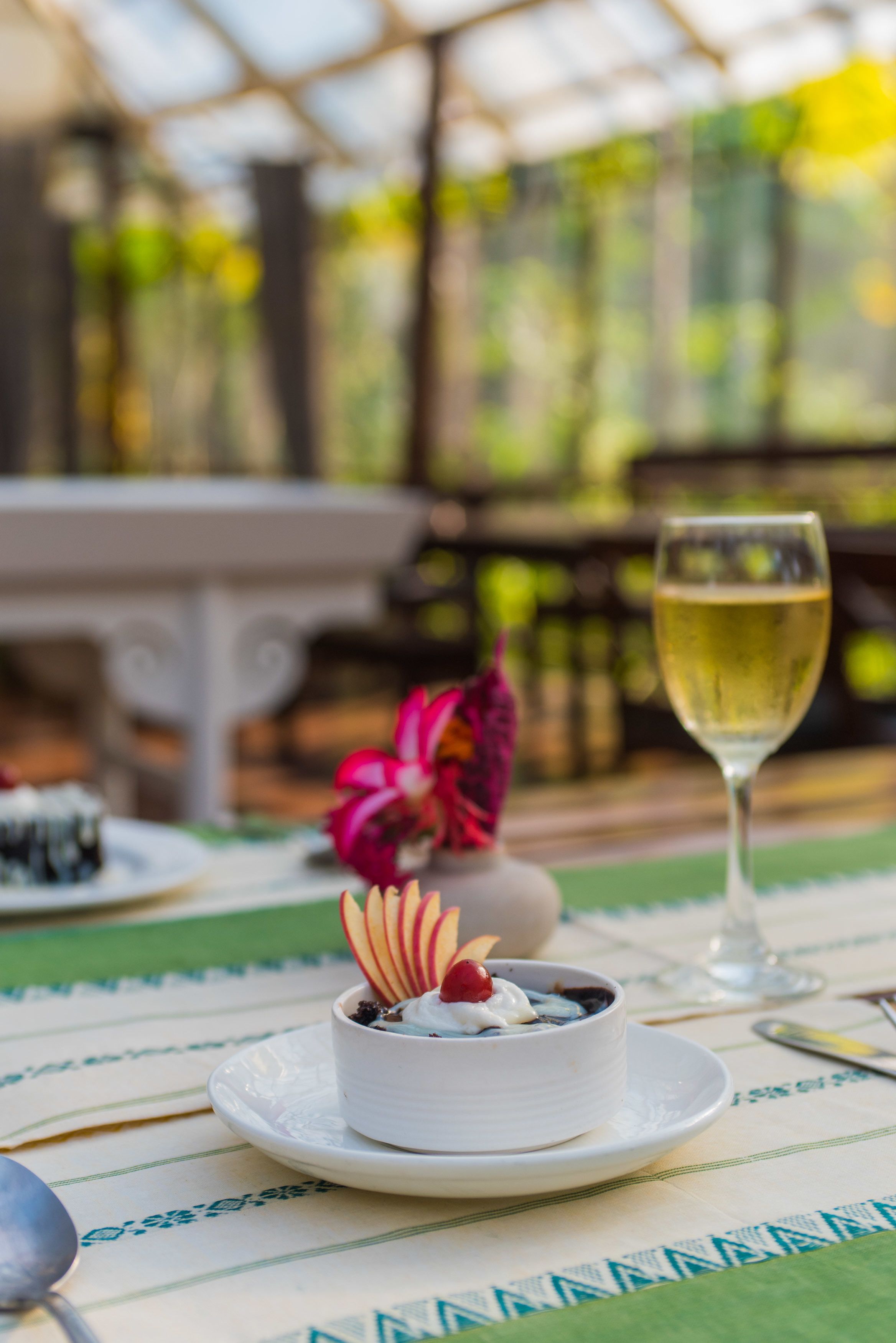 A dessert on a white plate with a glass of white wine beside it, set on a table with a patterned tablecloth.