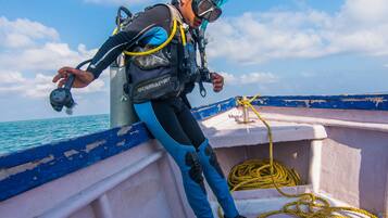 A diver with scuba gear leaning on a boat's edge, with the ocean and sky in the background.