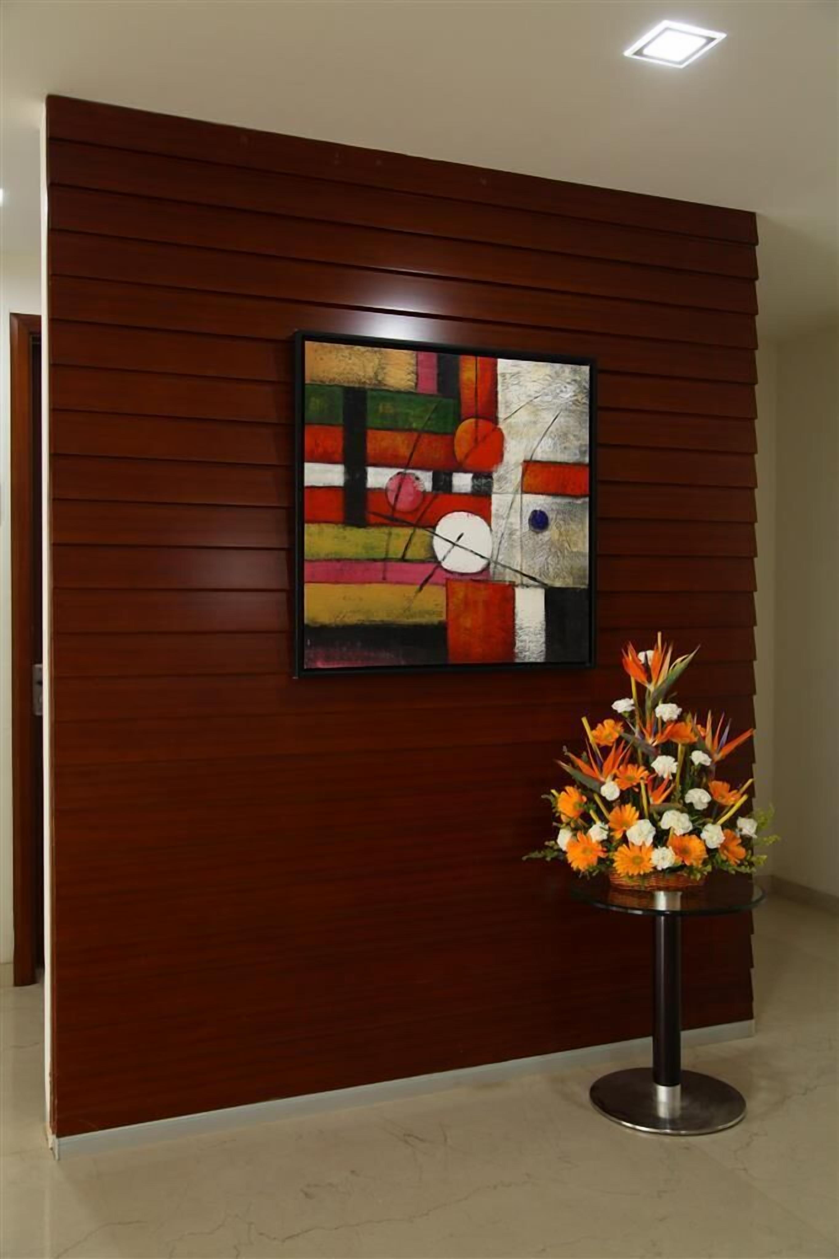 Un espace d’accueil avec un mur recouvert de panneaux en bois, une peinture abstraite aux couleurs vives et un arrangement floral sur une table.