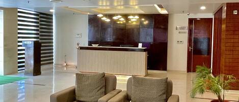 A modern lobby with a reception desk, seating area, and a potted plant.