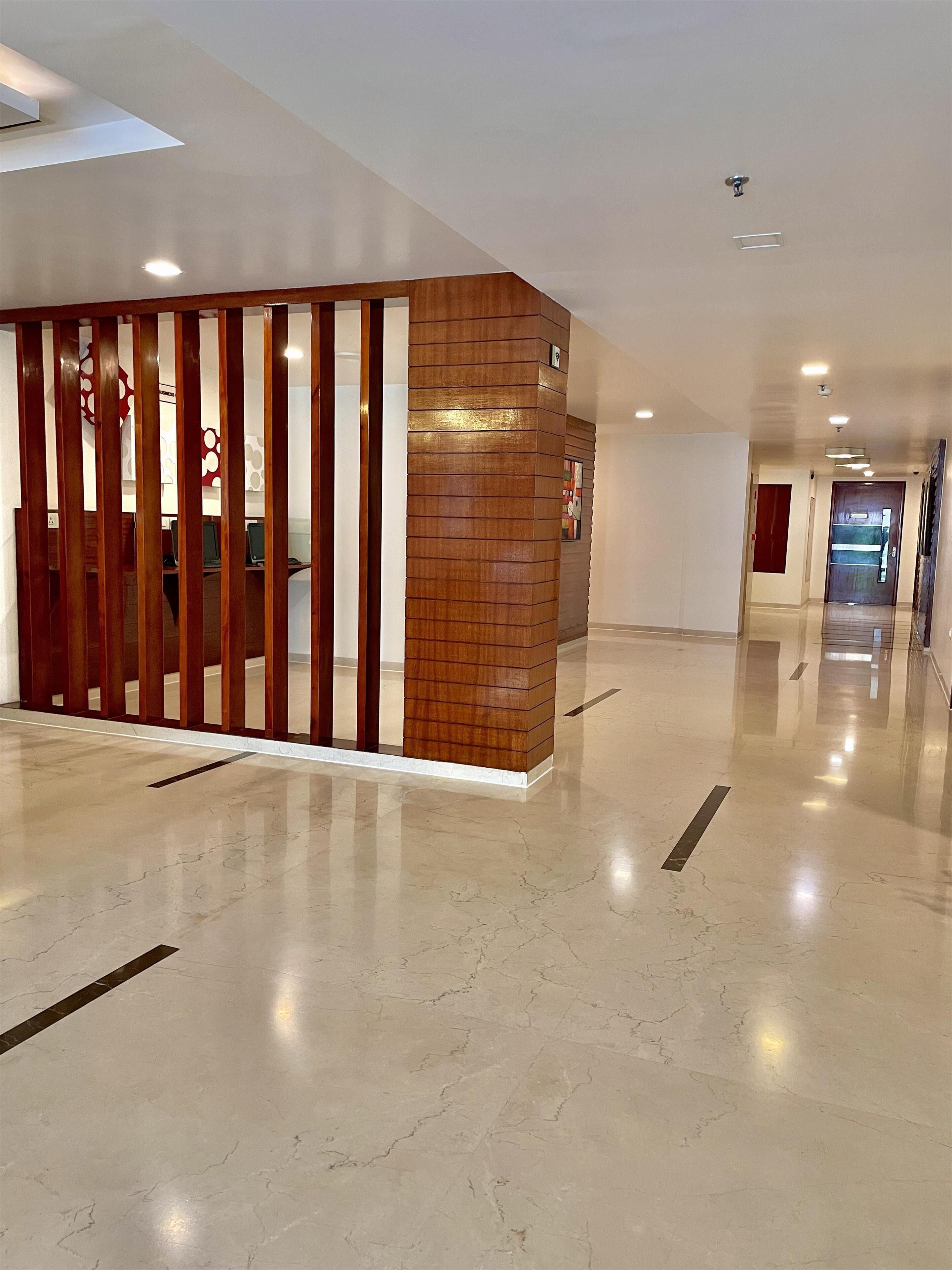 Un hall d’entrée spacieux et moderne, doté d’un sol en marbre poli, d’une cloison en bois à lattes verticales et d’un éclairage encastré au plafond.