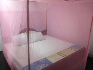 A single bed with a pink mosquito net, a white pillow, and a patterned bedspread. - Home Feel Home stay (Tangalle)