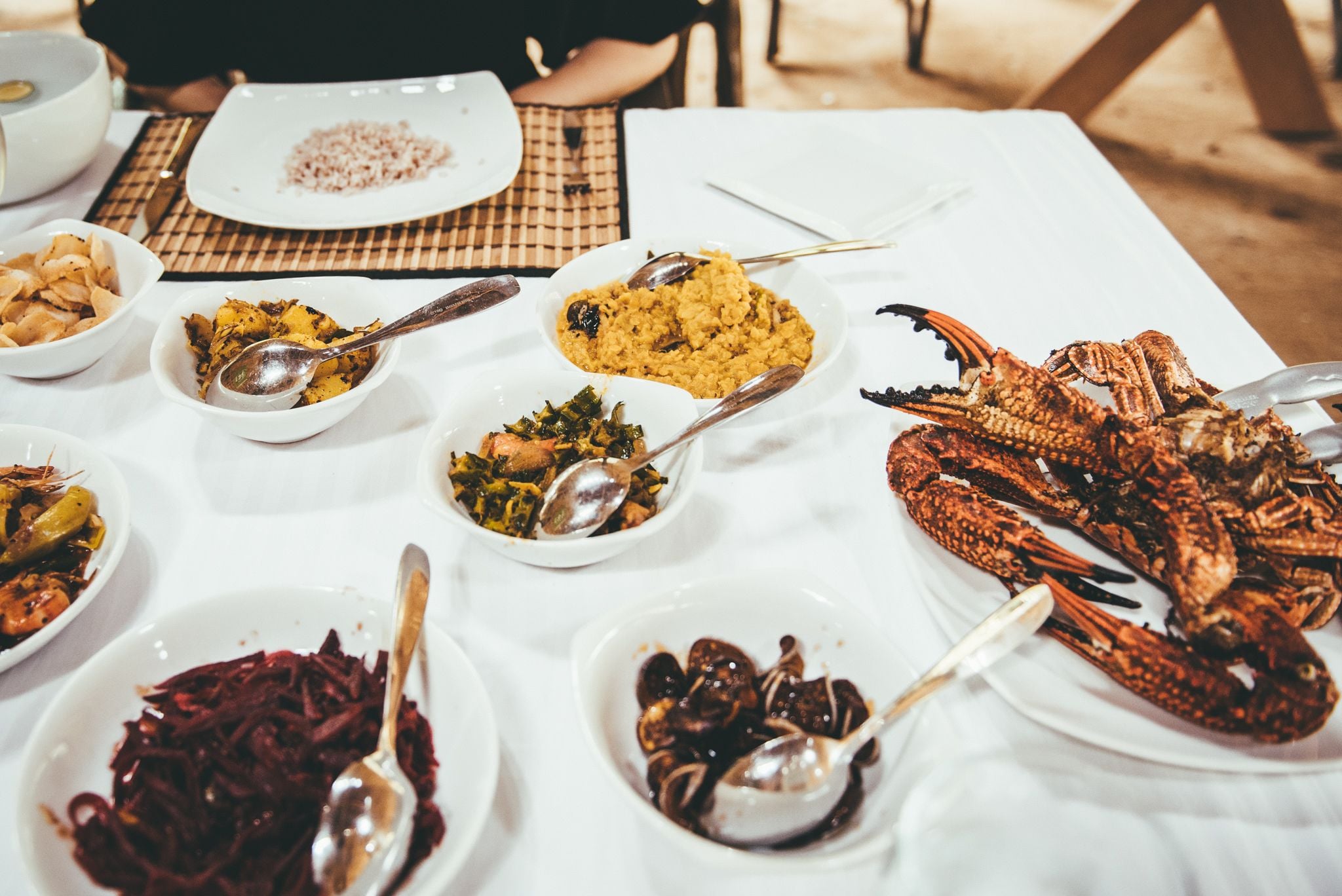 A table with various dishes including seafood and rice, with spoons on each plate.