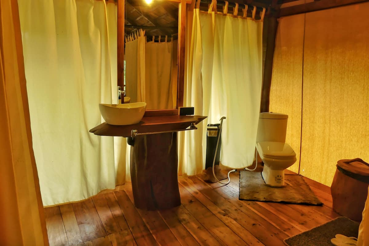 A bathroom with a wooden floor, a sink with a mirror, a toilet, and a shower curtain.
