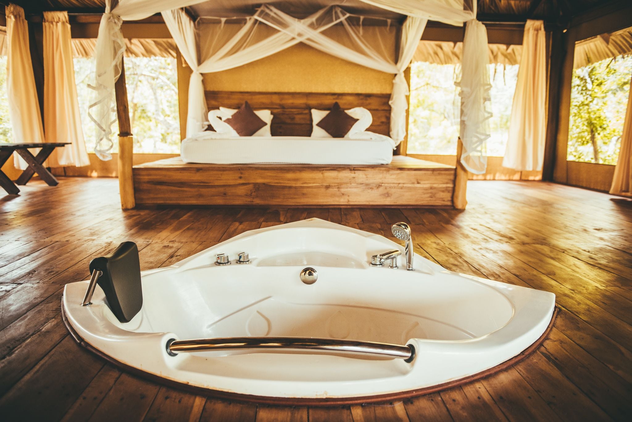 A bedroom with a large bathtub, wooden flooring, and a canopy bed.
