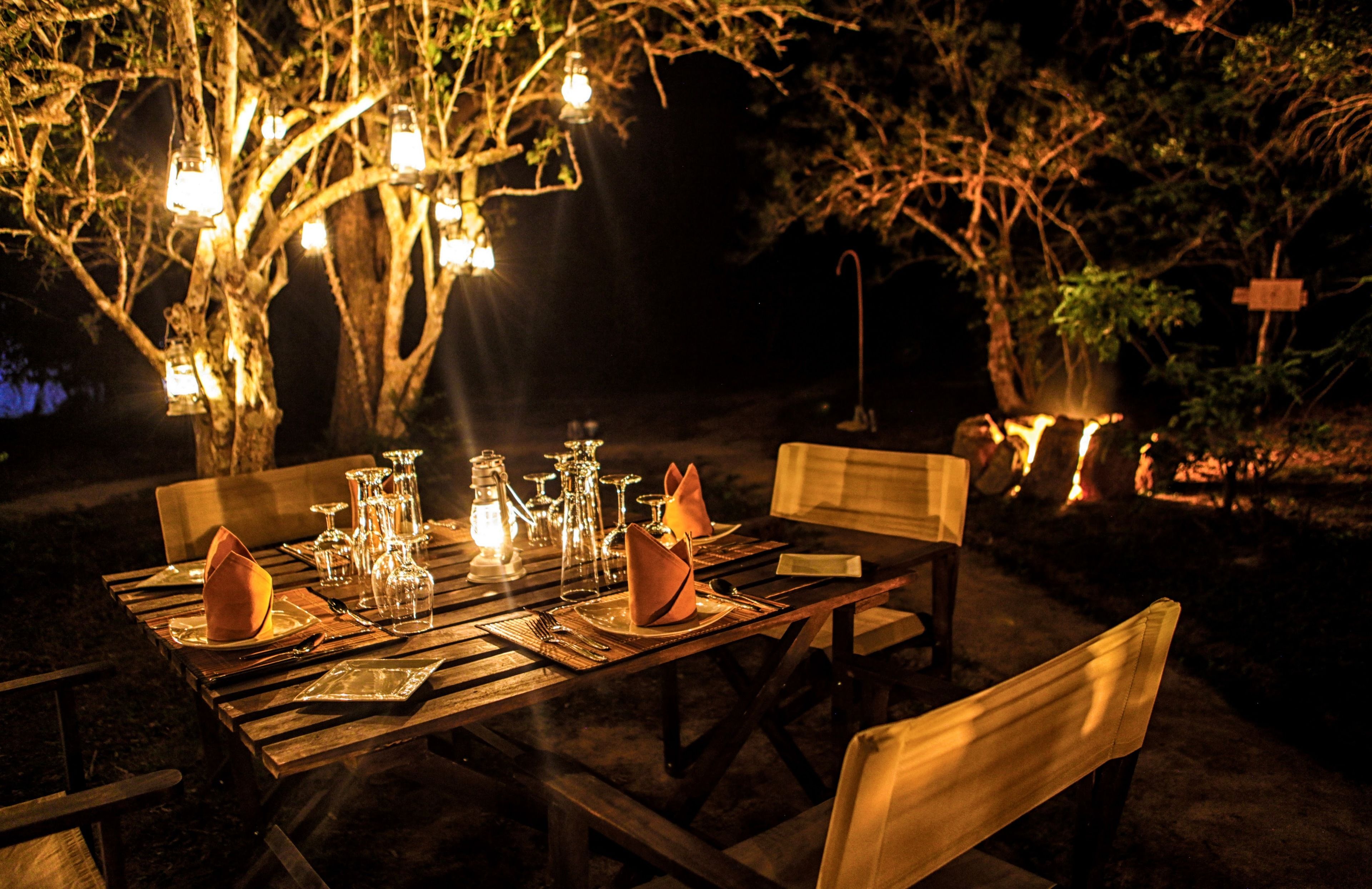 An outdoor dining area with wooden tables and chairs, set with glassware and napkins.
