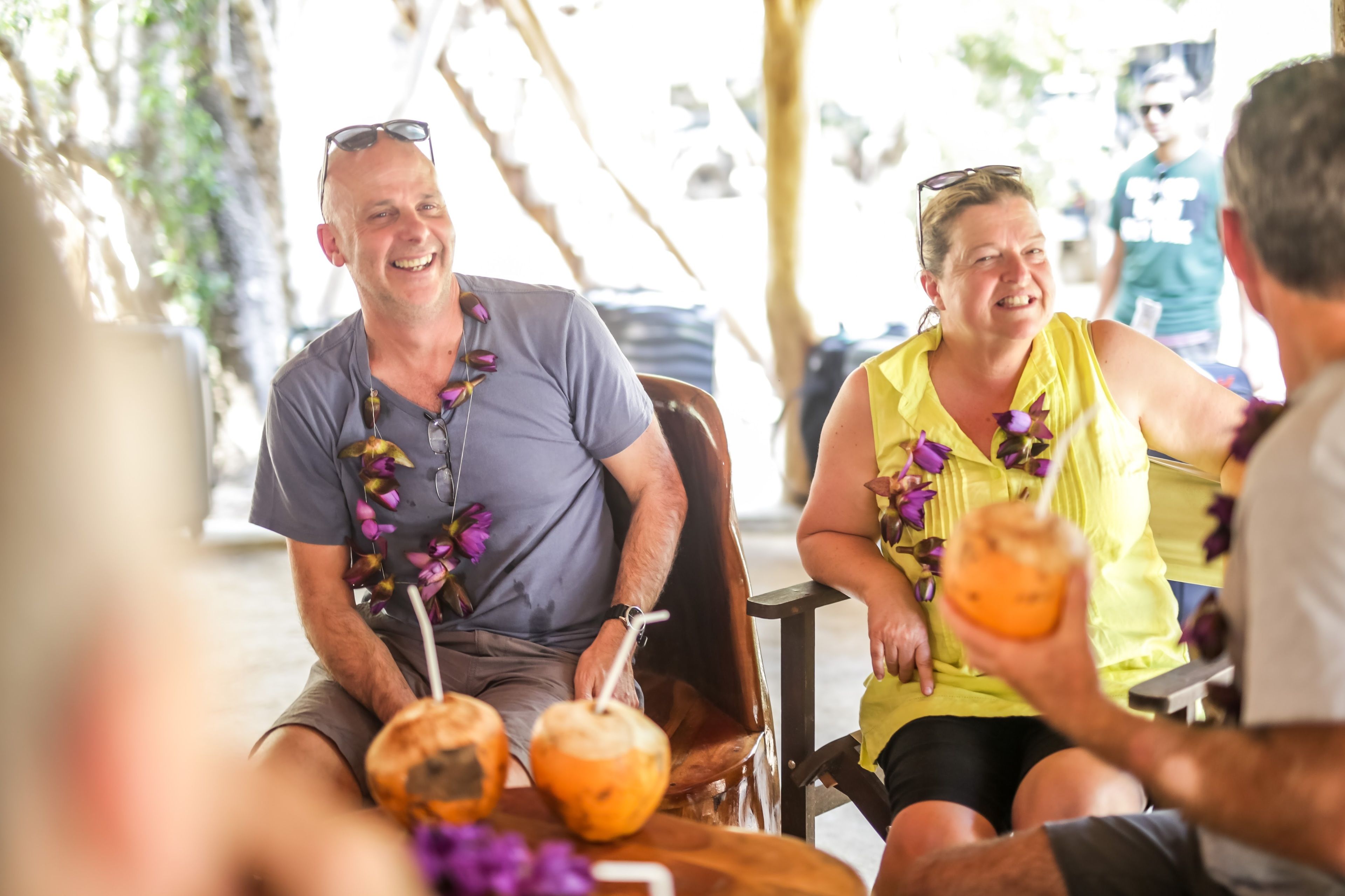 Un hombre y una mujer sentados a una mesa con bebidas, rodeados de decoraciones tropicales.