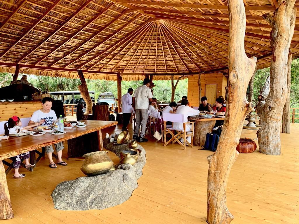 An outdoor dining area with a thatched roof, wooden tables, and rustic decor.