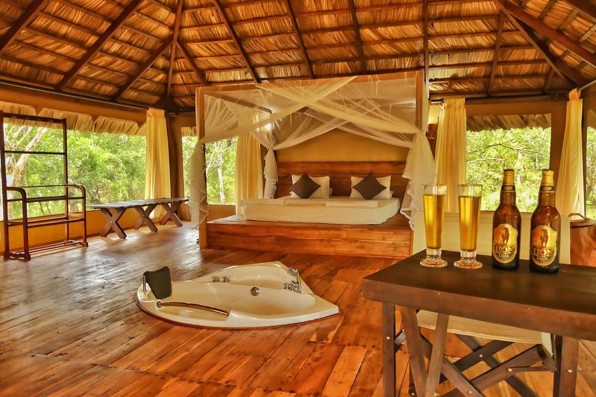 A wooden room with a bed, a table with drinks, and a bathtub.