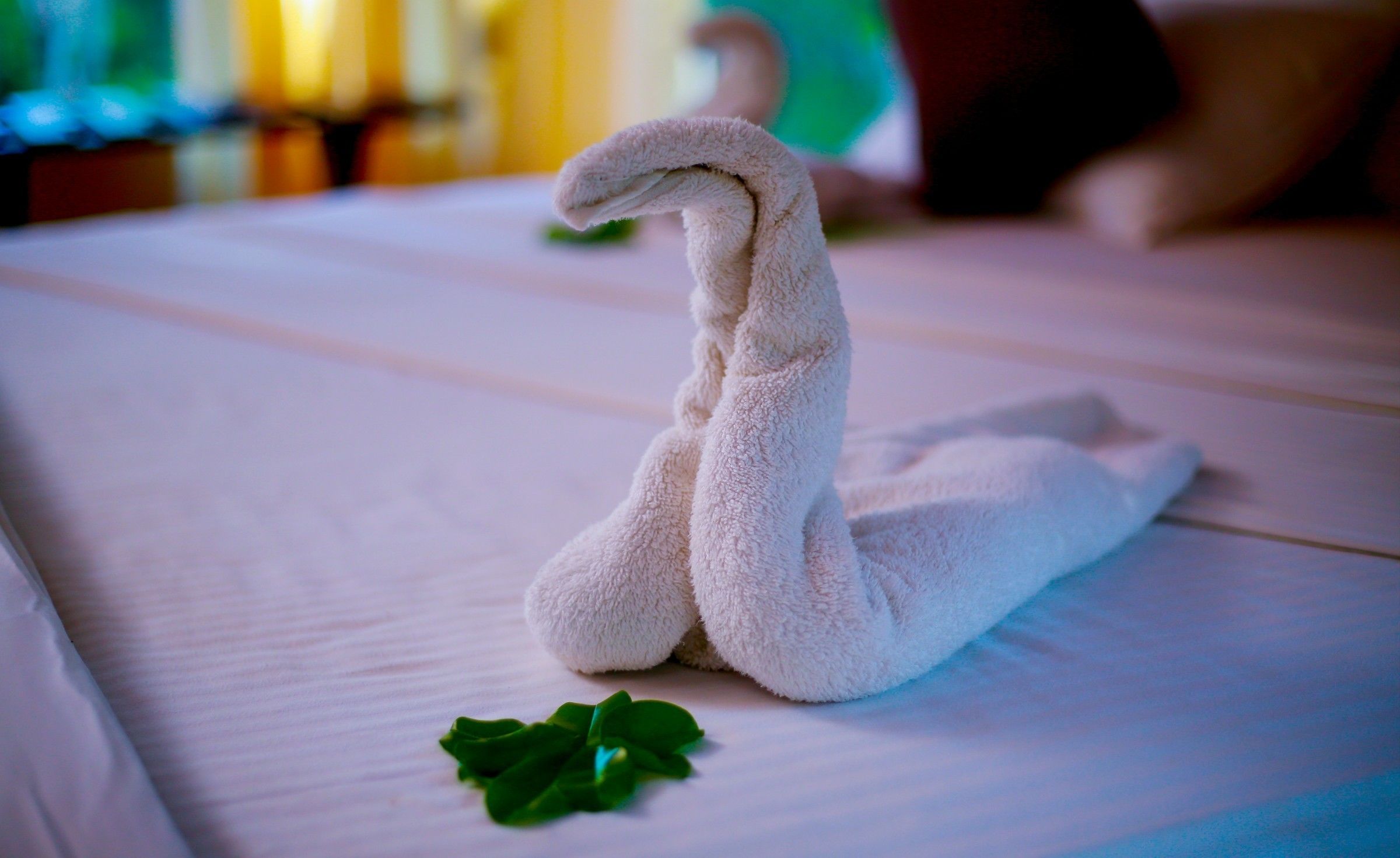 Une serviette en forme de cygne est posée sur un lit, avec une feuille verte à côté.