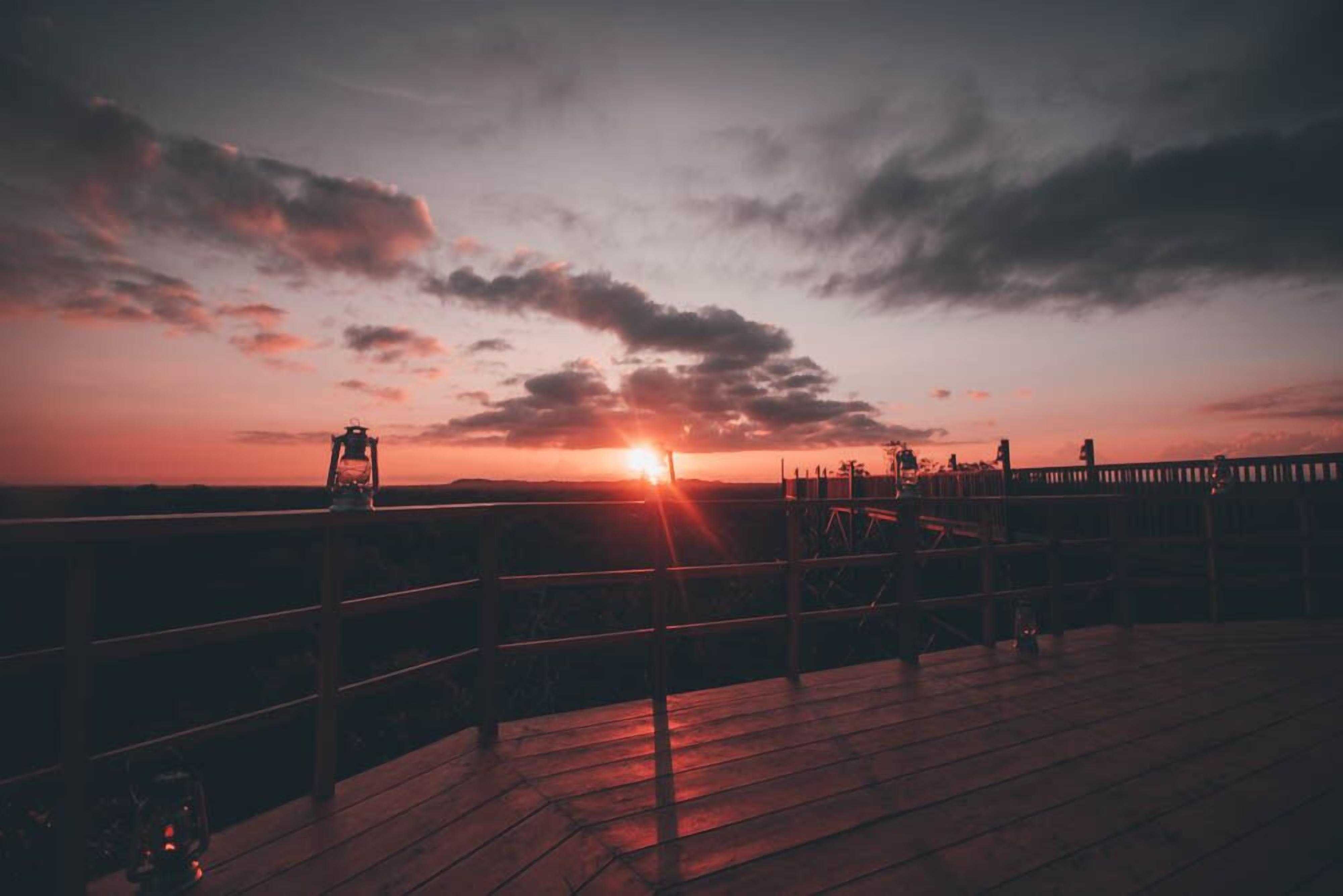 A sunset over a wooden deck with railings, a railing, and a lantern.