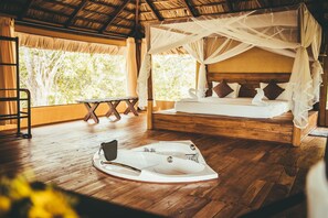 A room with a wooden floor, a bed with a canopy, a bench, and a bathtub. - Yala Safari Camping (Kataragama)