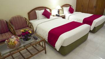 A hotel room with two beds, a small table with a basket of fruit and flowers, and a chair.