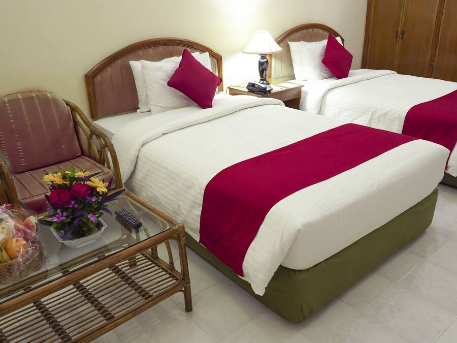 A hotel room with two beds, a small table with a basket of fruit and flowers, and a chair.
