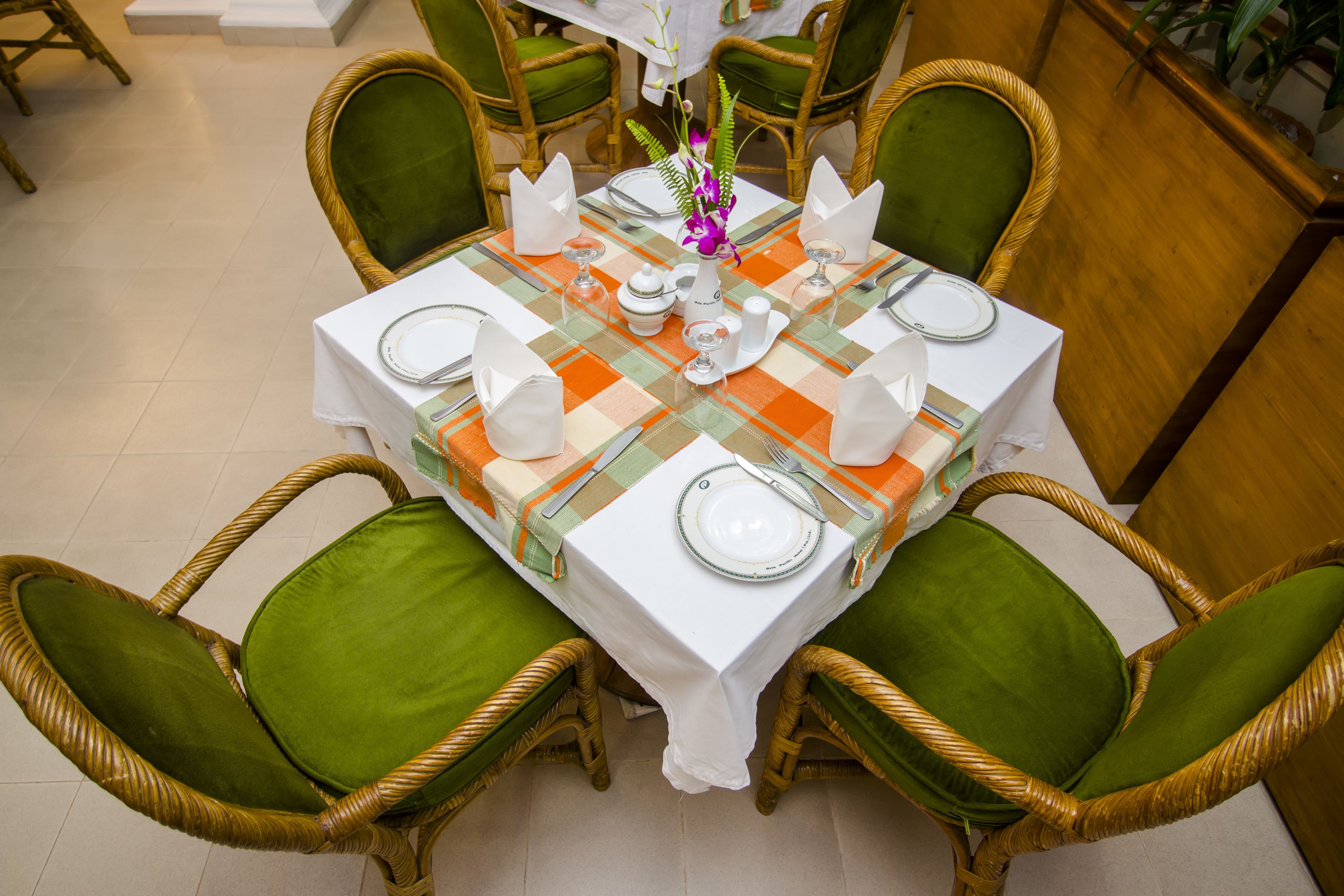 Uma mesa de jantar posta com pratos brancos, talheres e um vaso de flores.