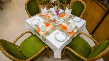 Uma mesa de jantar posta com pratos brancos, talheres e um vaso de flores.