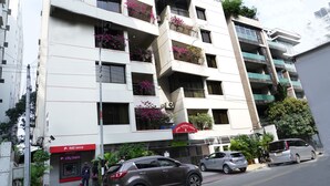 A multi-story building with balconies adorned with flowering plants, a visible bank branch, and parked cars on the street. - Asia Pacific Hotel (Dhaka)