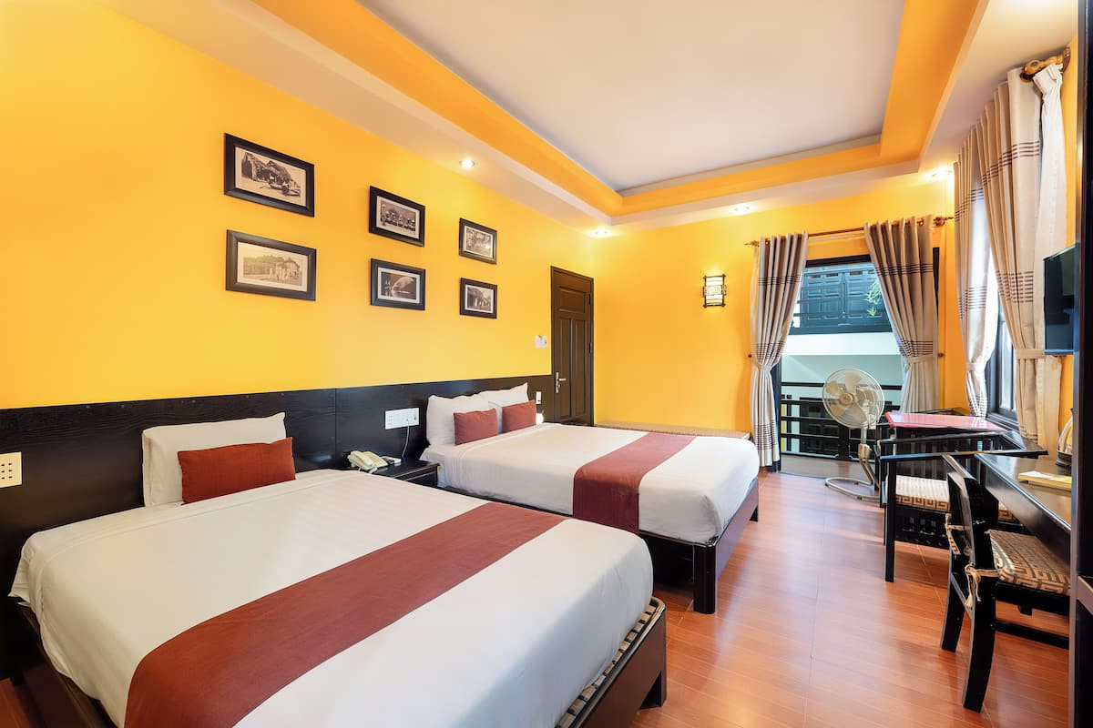A hotel room with two beds, a desk, a chair, and a balcony with a view.