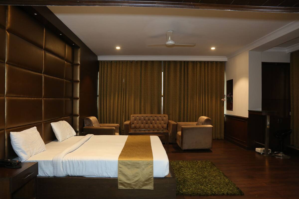 A hotel room with a large bed, two armchairs, a sofa, a television, and a ceiling fan.