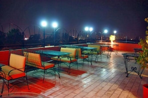Un espacio al aire libre con mesas y sillas, iluminado por luces colgantes.