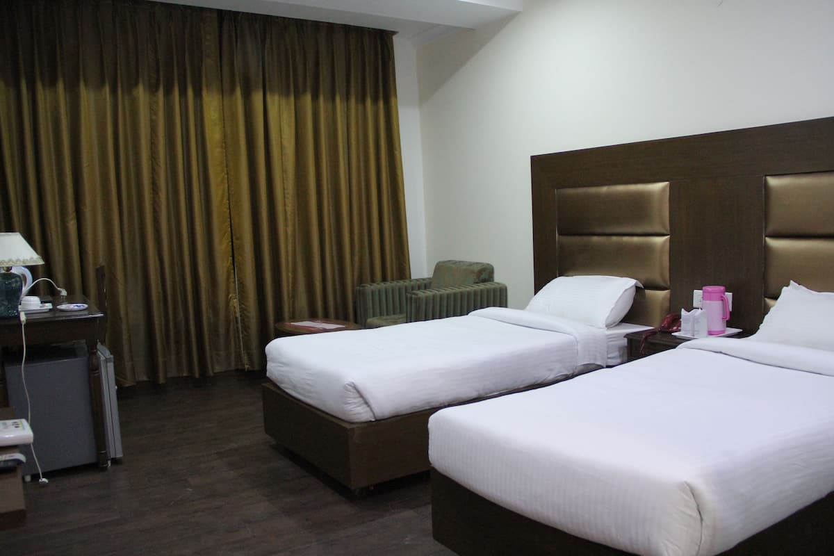 A hotel room with two beds, a desk with a lamp, a radiator, and a telephone.