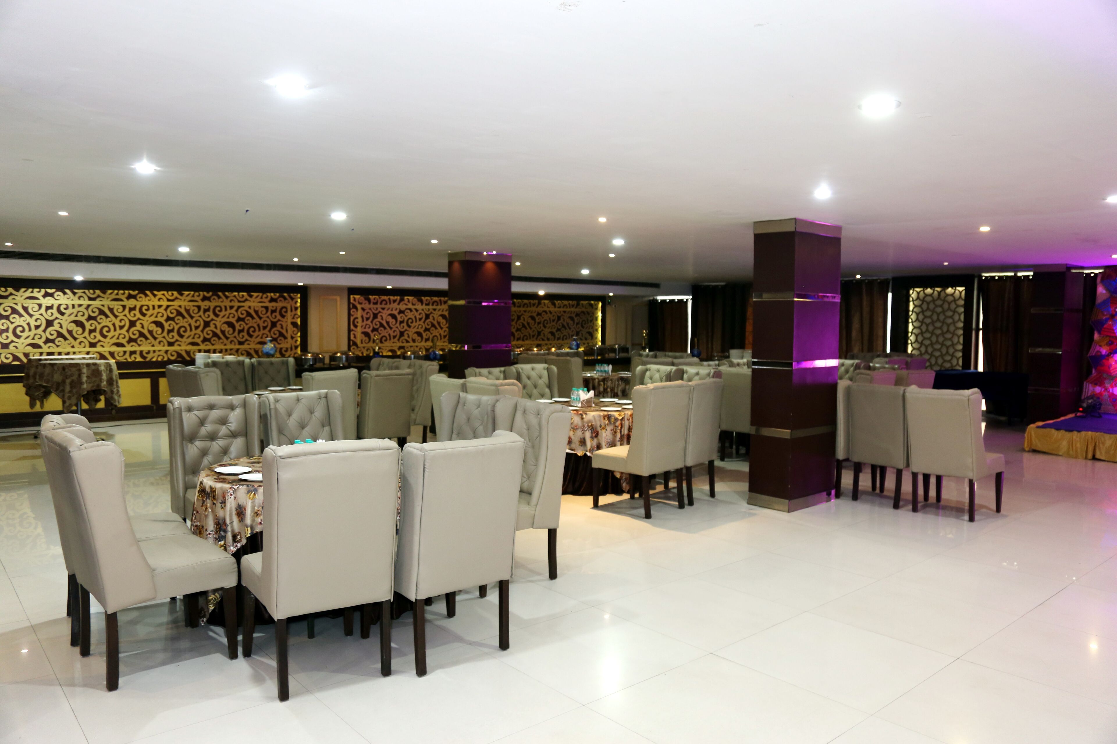 Un restaurante con varias zonas de comedor, incluyendo una sección con mesas y sillas redondas y otra con mesas y sillas cuadradas.