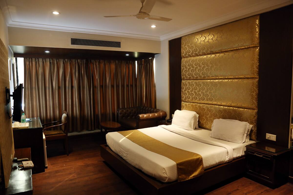 A hotel room with a large bed, a desk, a chair, and a ceiling fan.