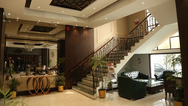 Vestíbulo de hotel con escalera, zona de estar y mostrador de recepción.