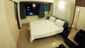 A hotel room with a large bed, a desk, and a window with curtains. - Tex-Palazzo Hotel (Surat)