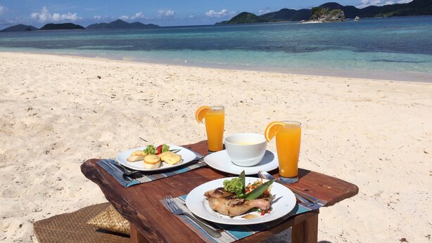 A wooden table with plates of food and drinks on a beach.
