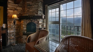 A cozy room with a stone fireplace, wicker chairs, and a large window offering a mountain view. - Provence Rose Lodge in Ching Jing (Ren'ai)