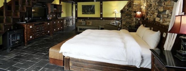 Une chambre confortable avec un grand lit, une cheminée et un mur en pierre.