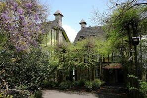 A traditional stone building with a steeply pitched roof, surrounded by lush greenery and purple flowering trees. - Provence Rose Lodge in Ching Jing (Ren'ai)