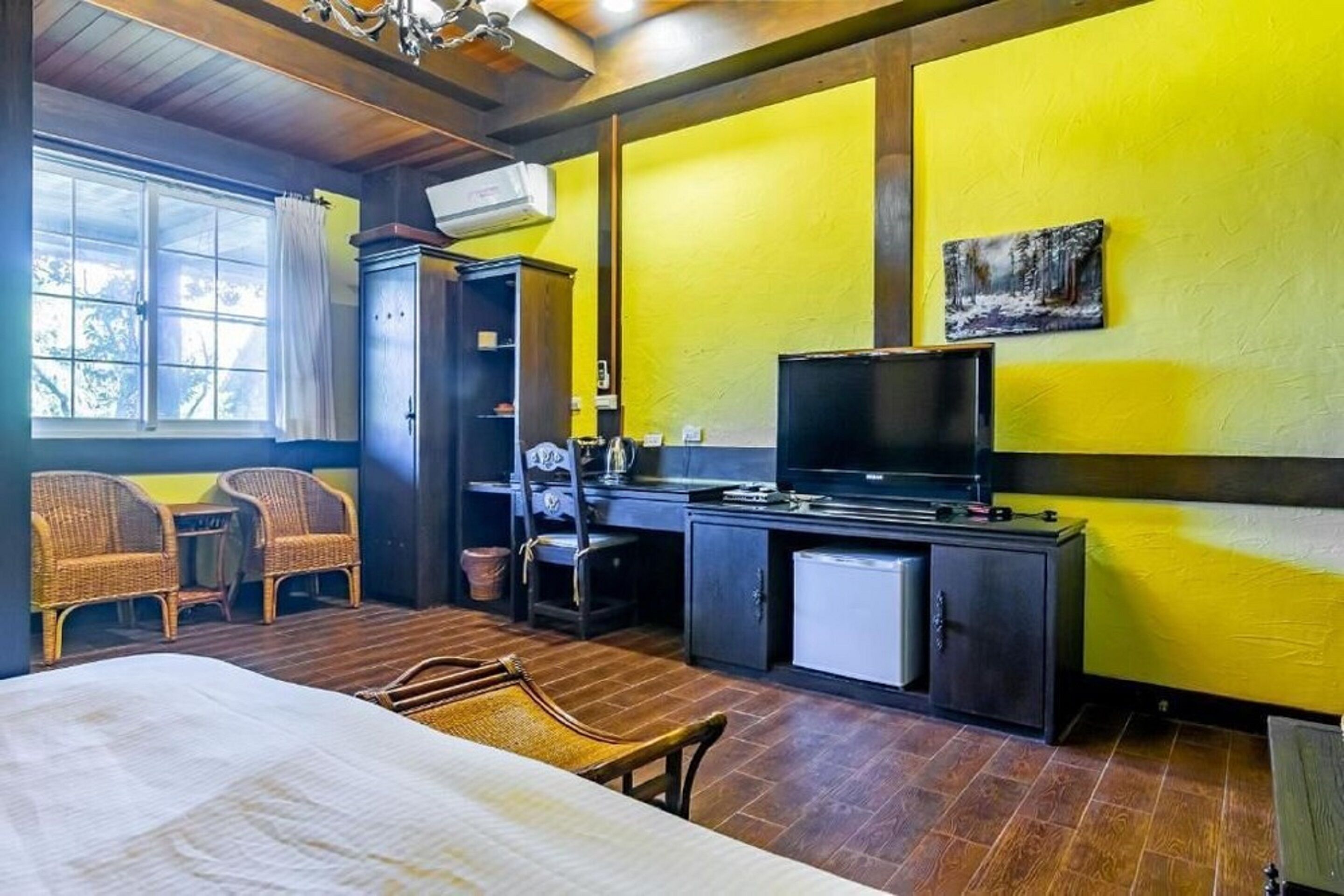 A room with a bed, a desk with a television, wicker chairs, and a small refrigerator.
