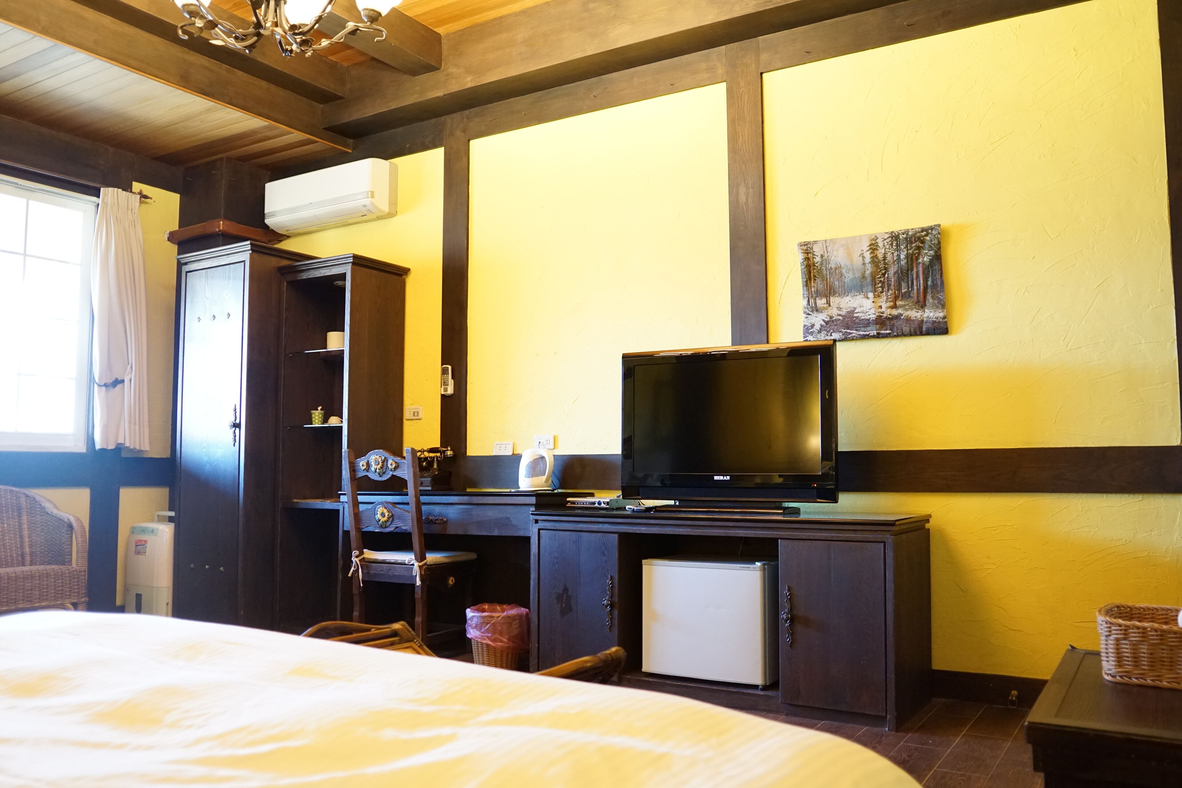 A hotel room with a bed, a desk with a television, a small refrigerator, and a window with curtains.