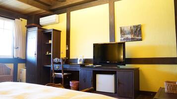 A hotel room with a bed, a desk with a television, a small refrigerator, and a window with curtains.