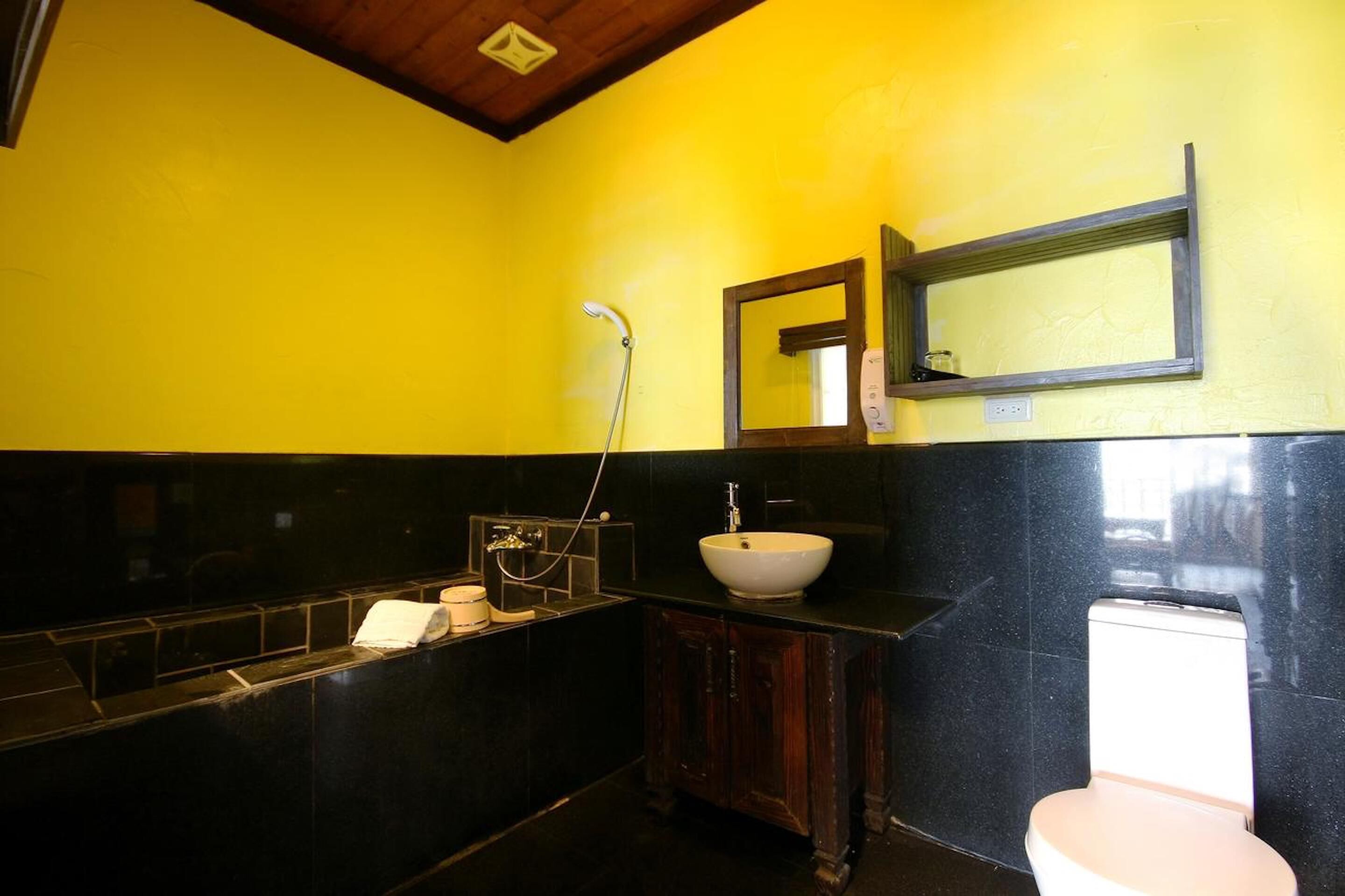 A bathroom with a yellow wall, a black sink, a white toilet, and a wooden cabinet.