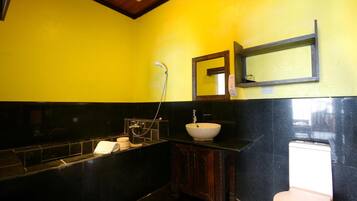 A bathroom with a yellow wall, a black sink, a white toilet, and a wooden cabinet.